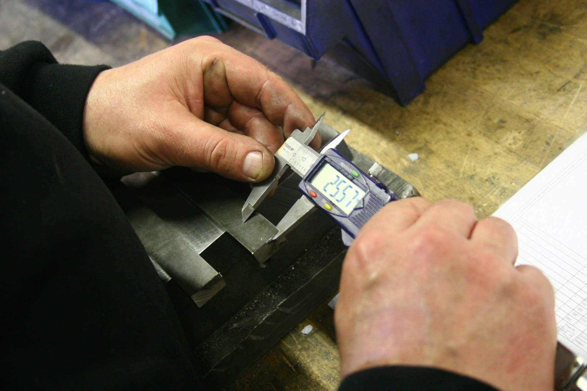 A worker checking a metal part with a caliper.